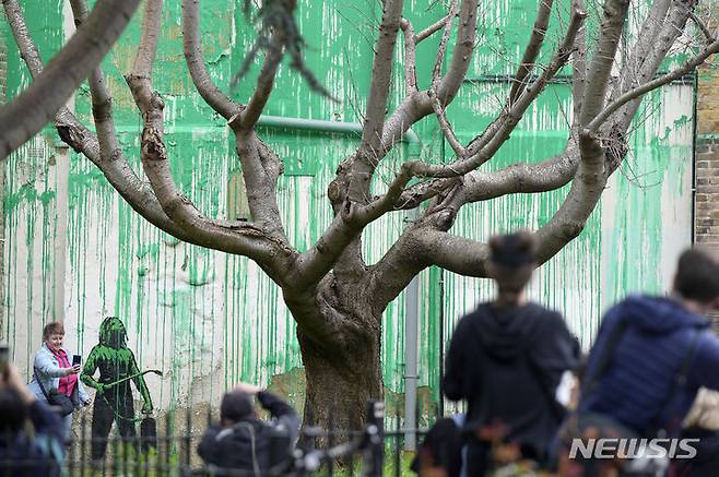 [런던=AP/뉴시스] 시민들이 18일(현지시각) 영국 런던 북부 핀스버러 공원 인근의 한 건물에 '얼굴 없는 화가'로 알려진 영국 유명 그라피티 작가 뱅크시가 그린 벽화를 보고 있다. 2024.03.19.