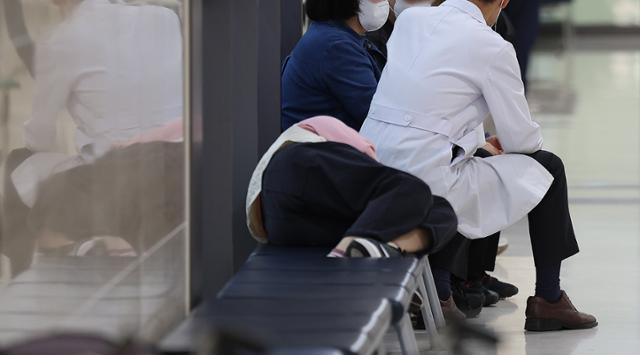 전공의 집단 이탈 사태가 계속된 27일 대구의 한 대학병원 병동 의자에서 환자와 면담하는 의사 오른쪽에 한 사람이 누워 있다. 대구=연합뉴스