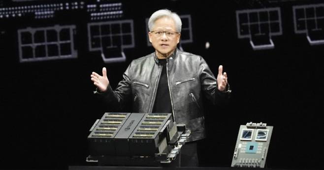 젠슨 황이 18일(현지 시간) 미국 캘리포니아 새너제이에서 열린 연례 개발자 행사 ‘GTC 2024’에서 인공지능(AI)용 차세대 그래픽처리장치(GPU)인 ‘블랙웰’ 시리즈를 소개하고 있다. 황 CEO 앞에 놓인 제품은 GPU 8개로 구성된 컴퓨팅 장치이고, 그의 왼쪽(사진 오른쪽)에 있는 것은 새로 출시한 블랙웰이 탑재된 기판이다. 그는 “세계에서 가장 강력한 칩으로 모든 산업에서 AI를 구현시킬 것”이라고 말했다. (새너제이=AP 뉴시스)