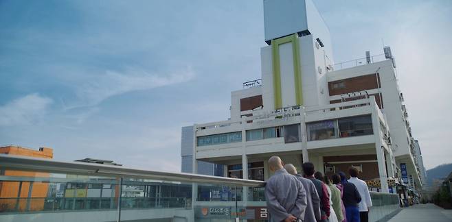 The "Vincenzo" cast look on at Geumga Plaza from the pedestrian walkway in a scene from the drama. (tvN)