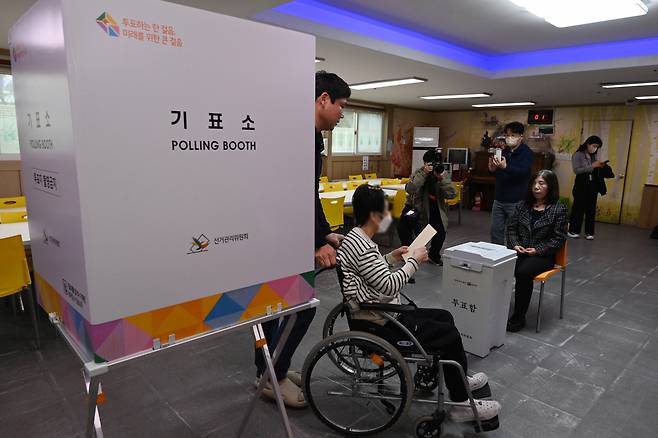 A woman in a wheelchair is pushed to a ballot box after voting at a rehabilitation facility for disabled people at Suwon, Gyeonggi Province on April 3. (Joint Press Corps)
