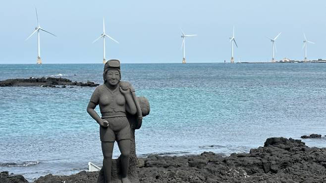 제주도 한경면 해안의 해녀 석상 뒤로 탐라해상풍력발전단지의 풍력 발전기들이 돌아가고 있다. 연합뉴스