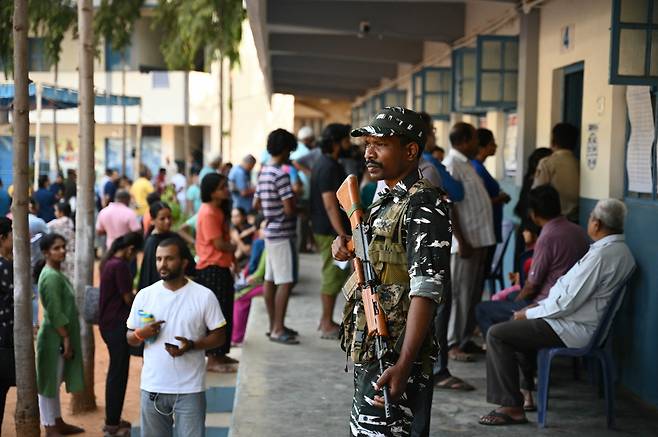 지난 26일(현지시간) 인도 벵갈루루에서 열린 인도 총선 2단계 투표에서 유권자들이 투표소 밖에서 투표를 하기 위해 줄을 서 있는 가운데 보안 요원들이 경비를 서고 있다. [AFP]
