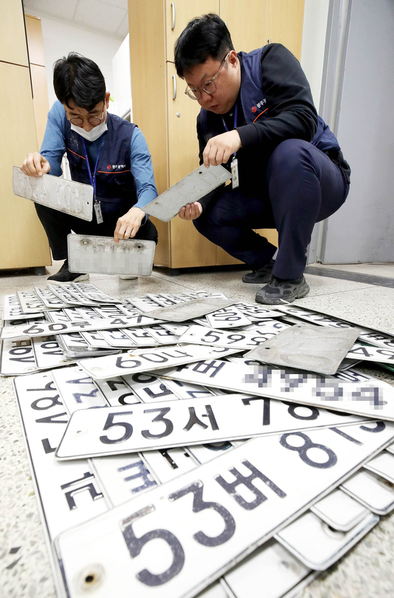 Employees from the delinquency management team at Gwangju's Buk District Office inspect license plates confiscated from delinquent vehicles on Monday. [YONHAP]