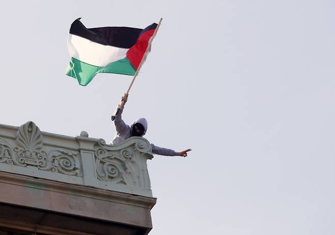 옥상서 펄럭이는 팔 국기 컬럼비아대 학생이 30일(현지시간) 팔레스타인 지지 시위 중 점거한 교내 해밀턴홀 옥상에서 팔레스타인 국기를 흔들고 있다. UPI연합뉴스