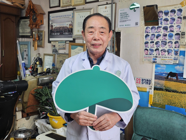 30여 년간 이발 봉사와 이웃 나눔을 지속해 온 문동호 후원자가 지난 3월 27일 자신이 운영 중인 충남 천안시의 동양이용원에서 그동안 정기 후원해 온 초록우산의 상징을 들고 서 있는 모습.  초록우산 제공