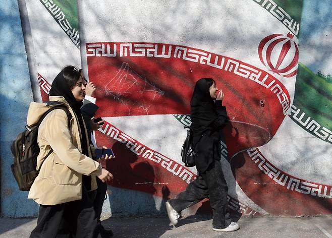 이란 청소년들이 2024년 2월13일 테헤란 거리의 이란 국기 벽화 옆을 걷고 있다. ⓒEPA 연합