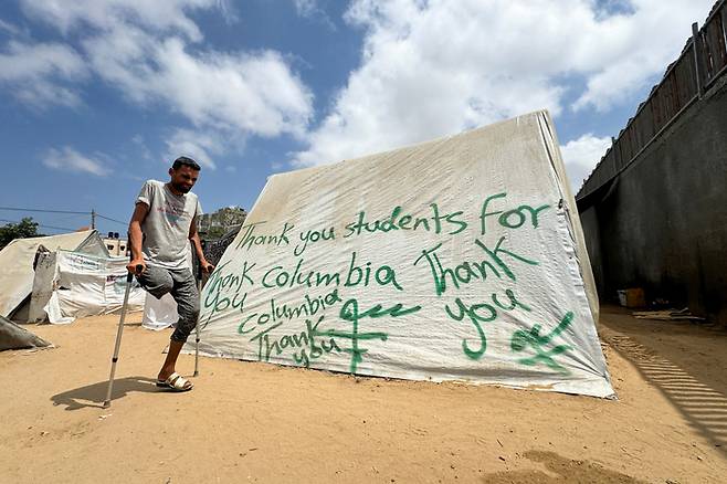 지난 2일(현지시간) 가자지구 최남단 도시 라파의 피란민 캠프에서 한 남성이 반전 시위를 벌이고 있는 미국 컬럼비아대학 학생들에게 고마움을 전하는 메시지가 쓰인 천막 앞을 지나고 있다. 로이터연합뉴스