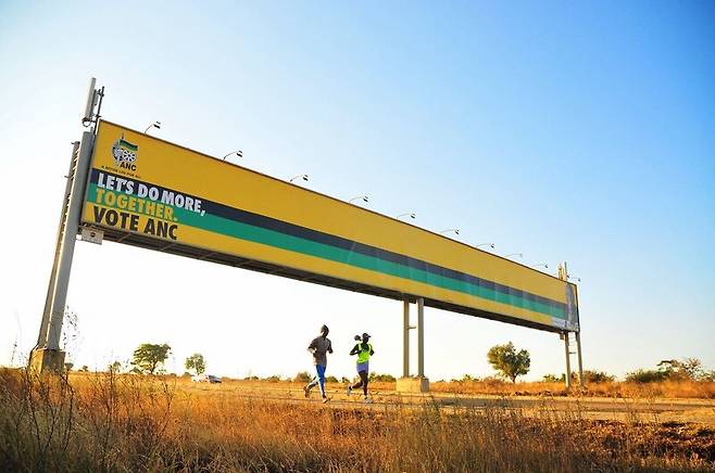 2일 남아프리카공화국 폴로콰네에서 조깅을 하는 이들이 아프리카민족회의 선거 광고판 아래를 지나고 있다. AFP 연합뉴스