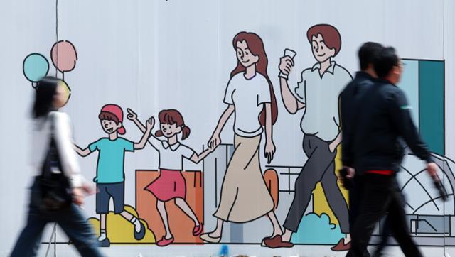 지난달 24일 오후 서울 도심의 공사장 가림막에 그려진 행복한 가족 그림 앞으로 시민이 지나가고 있다. 뉴스1