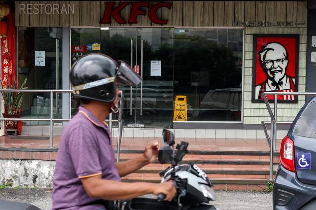 오토바이를 탄 말레이시아 시민이 지난달 30일 수도 쿠알라룸푸르에서 문이 굳게 닫힌 KFC 매장을 지나고 있다. KFC를 운영하는 QSR브랜즈 홀딩스는 매출 감소로 매장 108곳을 폐쇄했다. 쿠알라룸푸르=EPA 연합뉴스