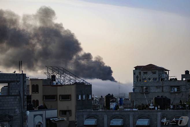 10일(현지시간) 동 트는 남부 가자 라파시 무너진 건물사이로 이스라엘군 포격에 당한 건물에서 뿜어져 나오는 검은 연기가 하늘을 덮고 있다. 이집트 중재로 진행되는 양측간 휴전 협상은 이날도 진전을 보지 못했다. 2024.05.10 ⓒ AFP=뉴스1 ⓒ News1 정지윤기자