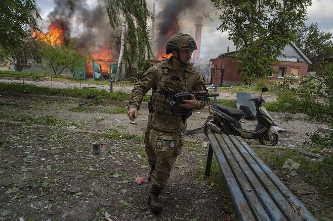 우크라이나 경찰이 러시아군이 진격해 치열한 전투가 벌어지고 있는 하르키우주 북부 국경 지역 보우찬스크에서 불타는 건물 앞을 지나고 있다. 보우찬스크/AP 연합뉴스