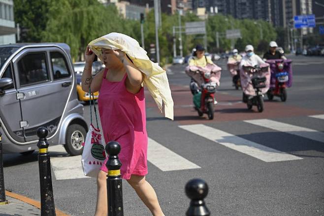 지난해 7월 19일 중국 베이징에서 한 시민이 겉옷을 벗어 햇볕을 가린 채 길을 건너고 있다. (사진=AFP)