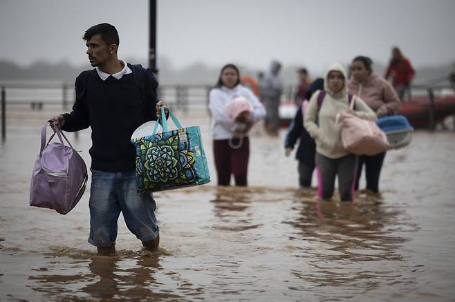 지난 3일(현지시간) 브라질 히우그란지두술주 포르투알레그레에 폭우가 내린 뒤 발생한 홍수로 고립된 주민들이 구조돼 물에 잠긴 거리를 걸어가고 있다. EPA연합뉴스