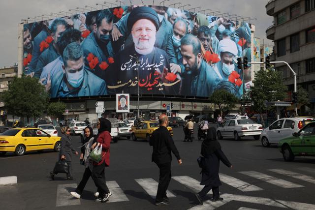 이란 시민들이 21일 수도 테헤란의 한 거리에서 19일 헬기 추락으로 사망한 에브라힘 라이시 이란 대통령의 사진이 붙은 광고판 앞을 지나고 있다. 로이터 연합뉴스