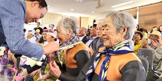지난 25일 오후 제주시 한림읍 귀덕2리어촌계회관에서 열린 사상 첫 해녀 은퇴식에서 양영철 제주국제자유도시개발센터(JDC) 이사장이 92살 김유생 해녀를 비롯한 9명의 해녀에게 스카프를 선물하고 있다. 연합뉴스