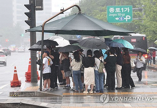 지난 5월 26일 오후 비가 내리는 서울 광화문광장에서 시민들이 파라솔 아래 우산을 쓴 채 보행신호를 기다리고 있다.  [연합뉴스]