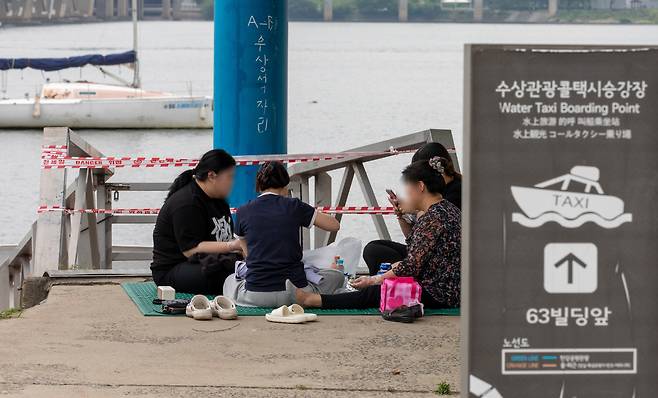 지난달 30일 서울 여의도 한강변에 설치된 수상택시 승강장 입구 앞에서 시민들이 자리를 깔고 앉아 음식물을 먹고 있다. 수상택시 승강장 주변은 철거를 앞두고 있어 한산한 모습을 보였다. /박성원 기자