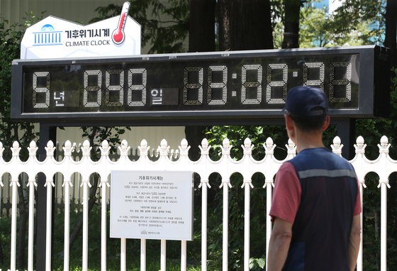 A passerby looks at a digital clock dubbed the Climate Clock installed in front of the National Assembly in Yeouido, western Seoul, on Tuesday, a day before World Environment Day. The clock shows that five years and 48 days are left until the Earth’s average temperature rises by 1.5 degrees Celsius (2.7 degrees Fahrenheit) compared to the pre-industrialized era or before the 20th century. [NEWS1]