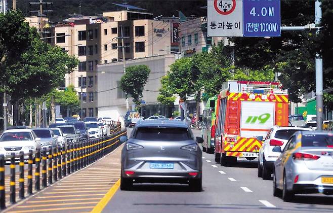서울시 119특수구조대 비상차량이 도로 중앙선에 ‘차선 도로 규제봉’ 플라스틱 말뚝을 설치한 종로구 평창문화로를 이동하고 있다. 차선 도로 규제봉은 비상시 출동하는 구급차나 소방차량의 장애물없이 길 중앙으로 이동하는 것을 불가능하게 막는 문제를 갖고 있다. [필자제공]