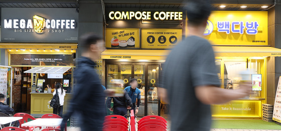 People pass by a cluster of takeout coffee shops located near Gwanghwamun Station in central Seoul on Sunday afternoon. [YONHAP]