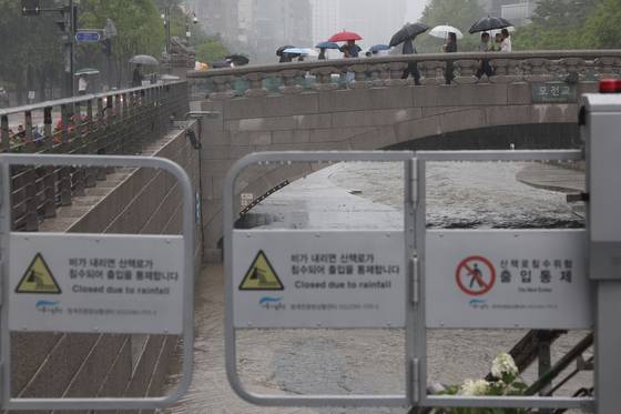 People walk past the Cheonggyecheon, a stream that flows through downtown Seoul, which was closed for safety reasons following a heavy rain advisory on Tuesday. [YONHAP]