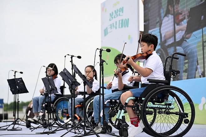 지난 5월 25일 하남 미사경정공원에서 열린 ‘2024 상상인 피크닉데이’에서 휠체어 사용 아동들이 ‘아카데미 상상인’을 통해 배운 바이올린을 연주하고 있는 모습.[사진 제공 = 상상인저축은행]