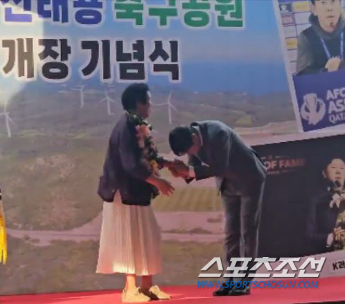 신태용축구공원 개장기념식에서 어머니의 목에 꽃다발을 걸어드린 후 허리 숙여 감사인사를 하고 있는 신태용 감독.