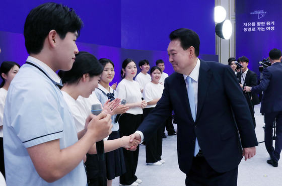 President Yoon Suk Yeol shakes hands with South and North Korean choir members during the commemoration of the inaugural North Korean Defectors' Day at the Blue House on Sunday. [JOINT PRESS CORPS]