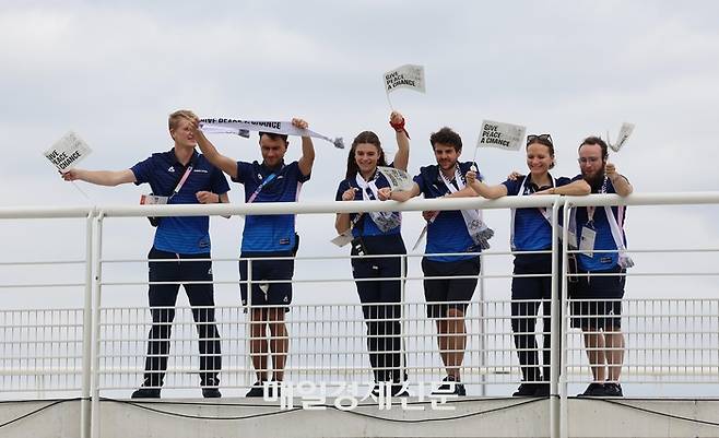 2024파리올림픽 개막을 나흘 앞둔 22일(현지시간) 파리 외곽 생드니에 위치한 올림픽 선수촌에서 열린 ‘평화를 위한 선수들의 외침’ 행사에서 자원봉사단원들이 ‘Give peace a chace’라고 적힌 손피켓을 흔들고 있다. 2024.7.22./생드니=이충우기자