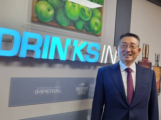 드링크인터내셔널 김일주 회장이 회사 로고 앞에서 포즈를 취하고 있다. 김 회장은 41년째 위스키 비즈니스를 하고 있는 위스키업계 대부다. /박순욱기자