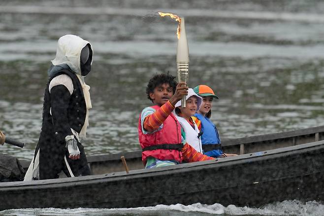 26일(현지시각) 열린 프랑스 파리 올림픽 개막식의 도입부, 프랑스 게임 '어쌔신 크리드'의 주인공 '아르노'(배 뒷쪽 남자)와 아이들이 센 강 위로 보트를 타고 성화를 나르고 있다. /AP연합뉴스