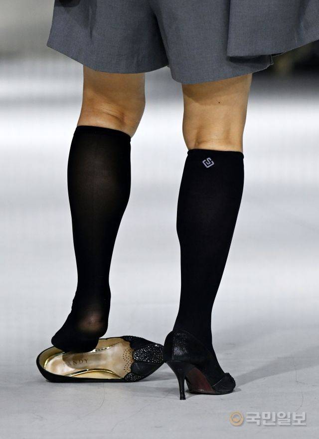 한 시니어모델이 패션쇼에서 구두가 벗겨져 다시 신고 있다.