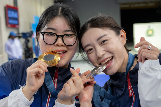 Oh Ye-jin, left, and Kim Ye-ji bite down on their gold and silver medal at the women's 10-meter air pistol final at the Chateauroux Shooting Centre in France on July 28. [JOINT PRESS CORP/HC]