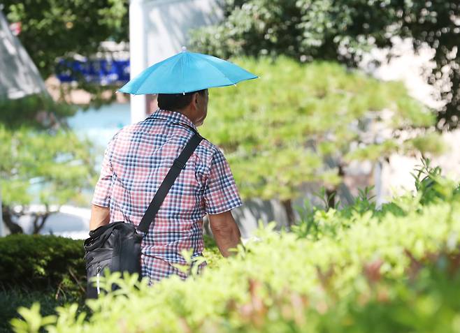 부산에 10일째 폭염경보가 이어진 5일 오후 부산 연제구 녹음공원에서 한 시민이 우산 모자로 햇빛을 가리며 이동하고 있다. /뉴스1