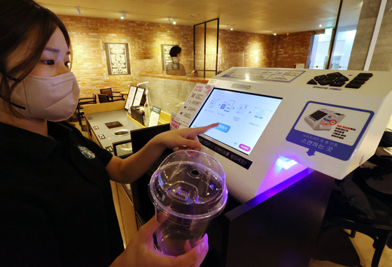 A staff member demonstrates the plastic cup recycling process at a Starbucks cafe in central Seoul on Tuesday. Recycling plastic cups using the dedicated kiosk in 42 selected cafes around the Gwanghwamun and Sungnyemun areas in central Seoul will reward the user with 100 won ($0.07). [YONHAP]