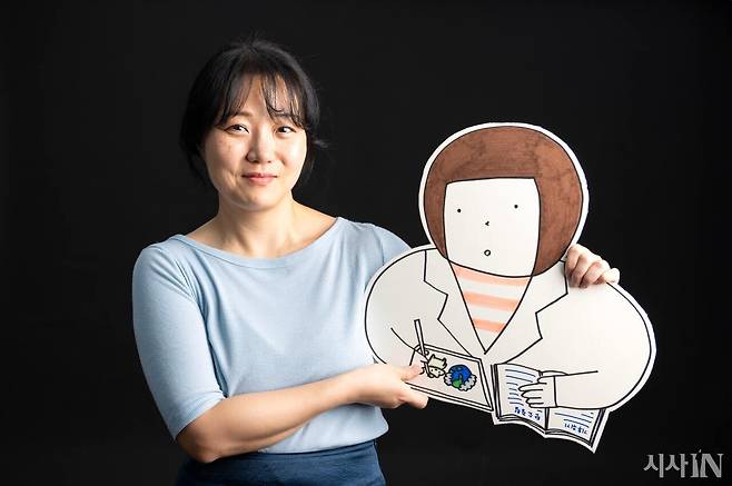 과학 일러스트레이터 이솔 작가가 동명의 캐릭터 ‘이솔’을 들고 있다. 약사 가운을 입고 과학 일러스트를 그리고 있는 모습이다.&nbsp;ⓒ시사IN 조남진