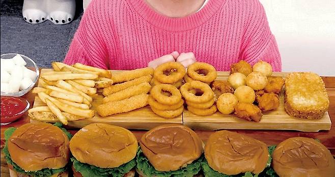 한 여성 유튜버가 수제버거 여러개와 튀김류를 한꺼번에 먹어보이는 컨텐츠를 방송하고 있다. 한국에선 유독 이런 대식 괴식형 먹방이 유튜브와 소셜미디어의 주요 컨텐츠로 인기를 끈다. /유튜브 캡처