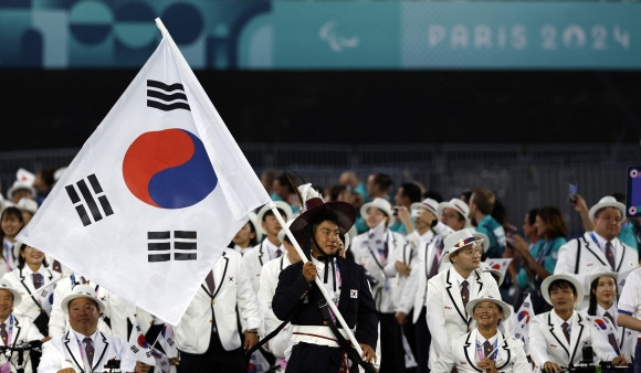 ‘패럴림픽’ 팀코리아 36번째 입장 - 한국 국가대표 선수단이 29일(한국시간) 프랑스 파리 콩코르드 광장에서 열린 2024 파리패럴림픽 개회식에서 36번째로 입장하고 있다. 기수로 나선 최용범(카누)은 특수 제작한 감색 외투와 문무 고위 관리들이 왕의 행차 시 썼던 붉은 갓을 착용했다. 그의 재킷에는 조선 태조 이성계가 입었던 곤룡포의 오조룡을 재창조한 금박 자수가 새겨졌다. 파리 AP 연합뉴스