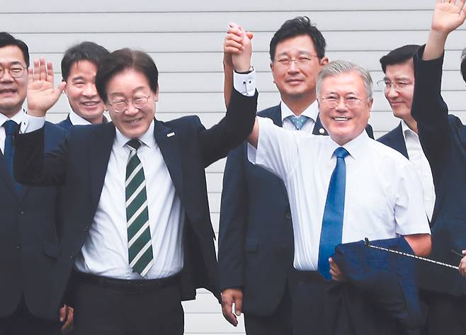 Democratic Party (DP) leader Lee Jae-myung, left, holds hands with former President Moon Jae-in following their meeting in Pyeongsan Village, South Gyeongsang, on Sunday. [NEWS1]