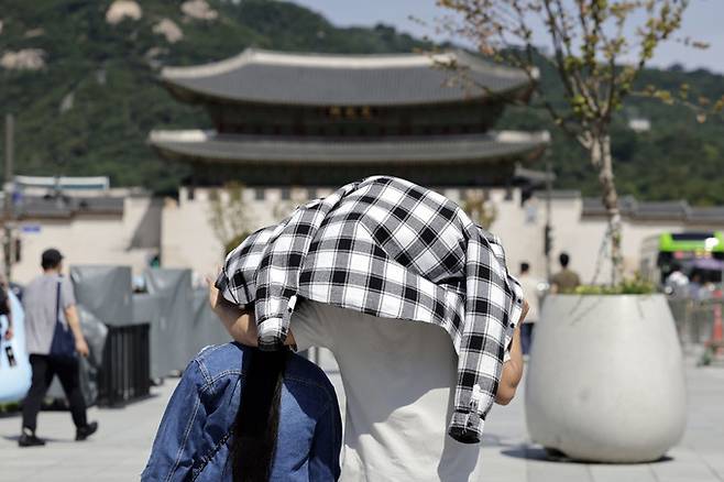 추석 연휴 폭염이 이어지고 있는 16일 서울 광화문 광장에서 외국인들이 뜨거운 햇살에 옷으로 얼굴을 가린 채 걷고 있다. 뉴시스