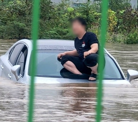 지난 21일 호우특보가 발효된 경남 김해에서 도로가 침수돼 한 남성이 차량 위로 대피해있다. 아래엔 흙탕물이 높게 차올라 차량 보닛이 거의 다 잠긴 상태다. 사진=뉴스1