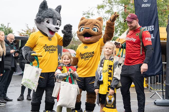 지난 15일(현지 시각) 영국 ‘몰리뉴 스타디움’ 앞 '치즈맛 불닭볶음면' 등 한국 스낵 보따리를 받아든 울버햄튼 원더러스 FC 팬들이 늑대 마스코트 인형 옆에 서 있다. /한국농수산식품유통공사(aT) 제공