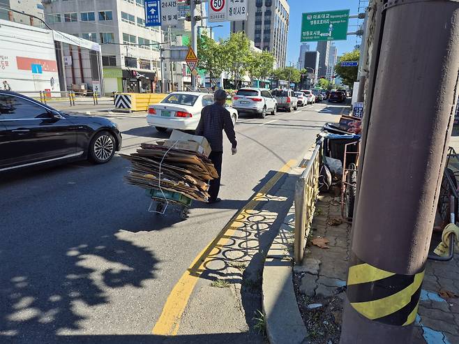 차도를 통해 고물상을 향해 걸어가고 있는 폐지수집 노인 모습. 형광조끼를 착용하지 않고 있다.[김도윤기자]