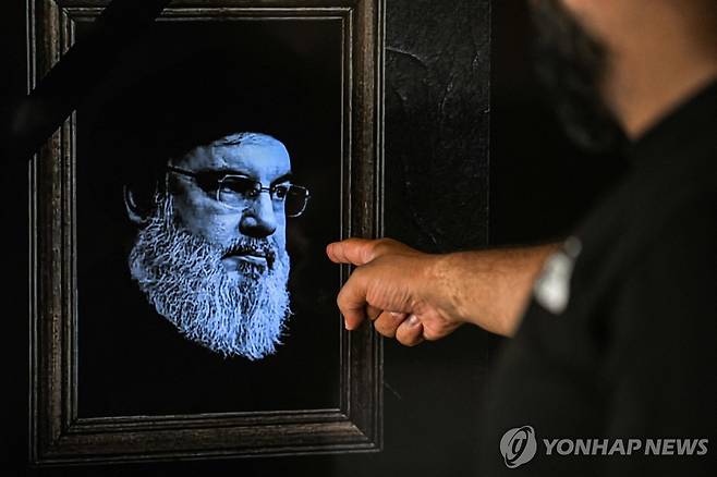 숨진 헤즈볼라 수장 하산 나스랄라 (AFP 연합뉴스) 28일(현지시간) 레바논 베이루트에서 한 남성이 이스라엘군 공습에 숨진 헤즈볼라 수장 하산 나스랄라의 영정이 표된 TV 화면을 가리키고 있다. 2024.9.29 dk@yna.co.kr