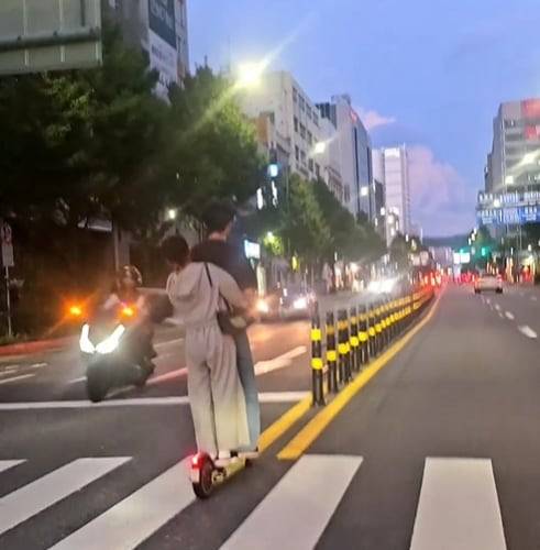 A couple rides an electric scooter against traffic without wearing helmets in this video grab from an online community.