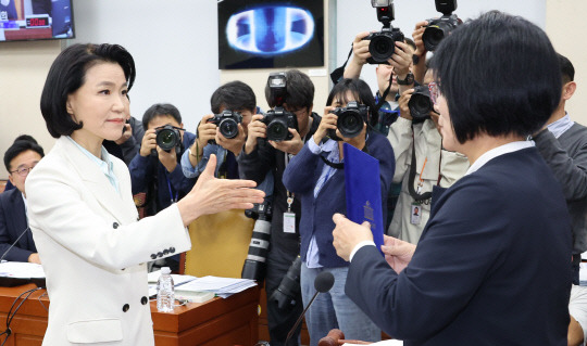 이진숙 방송통신위원장이 7일 오후 국회 과학기술정보방송통신위원회의 국정감사에서 최민희 위원장에게 증인선서문을 전달 후 악수를 먼저 청하고 있다. 이 위원장은 야당이 단독 처리한 탄핵소추로 직무가 정지된 상태라 기관 증인이 아닌 일반 증인으로 출석했다. [연합뉴스]