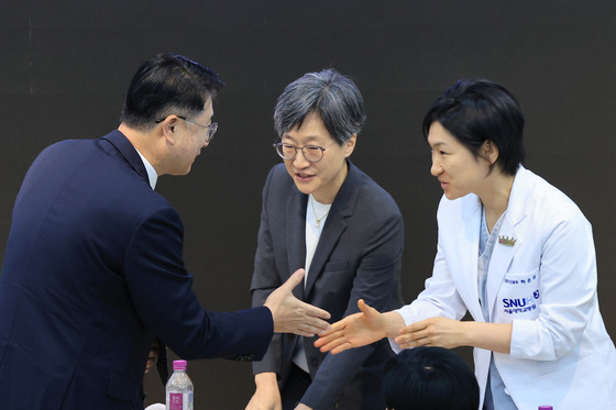 Jang Sang-Yoon, left, senior presidential secretary for social policy, shakes hands with Ha Eun-jin, a neurology professor at Seoul National University Hospital, after ending a public debate in central Seoul on Thursday. The person in the center is Kang Hee-gyung, a pediatric professor and head of the emergency response committee representing faculty at Seoul National University's College of Medicine. [YONHAP]