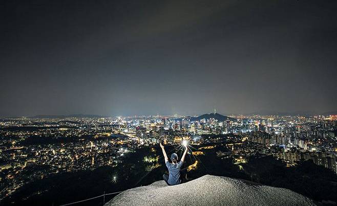 서울 도심 야경과 남산타워까지 파노라마처럼 감상할 수 있는 인왕산 범바위에 올라 사진 찍는 등산객. 한국에 푹 빠진 외국 MZ들 사이에선 이런 서울 도심 야간 등반 인증샷이 큰 인기라고 한다. /조선일보DB